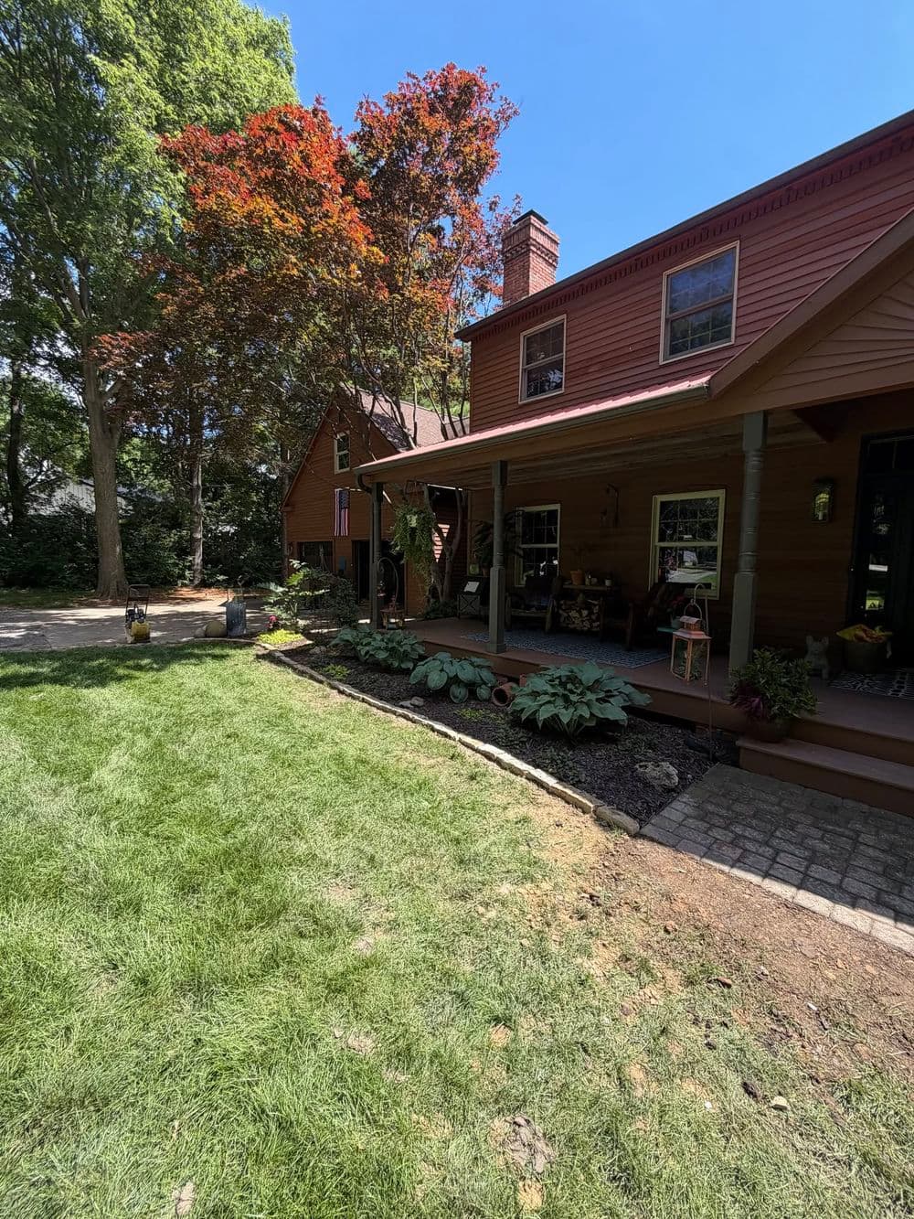 Cozy brown house with porch, vibrant red maple tree, and lush green lawn on sunny day.